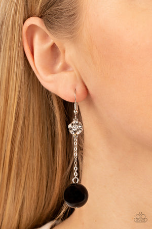  oversized black bead swings from the bottom of a dainty silver chain that is suspended from a white rhinestone encrusted silver bead