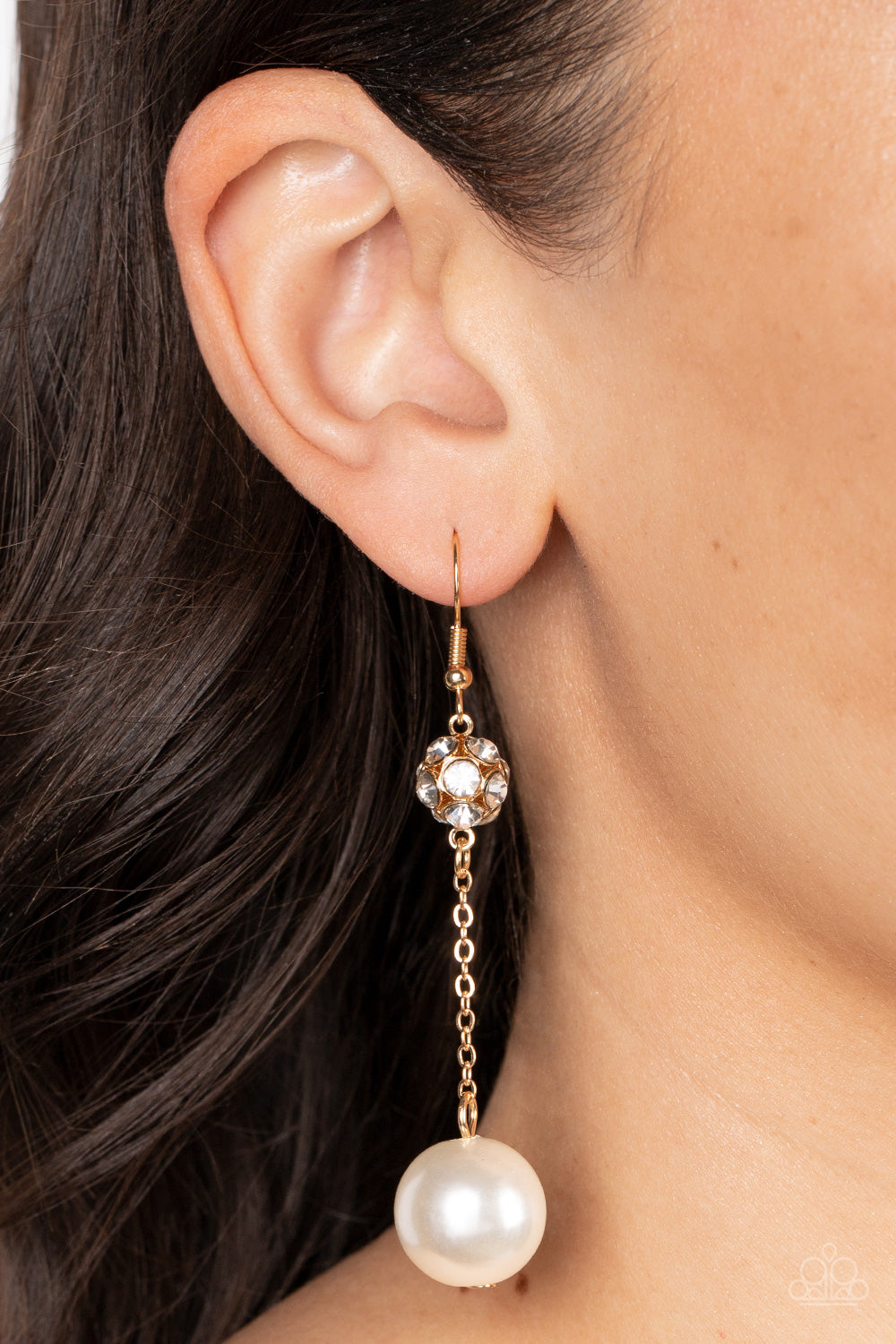 oversized white pearl swings from the bottom of a dainty gold chain that is suspended from a white rhinestone encrusted gold bead