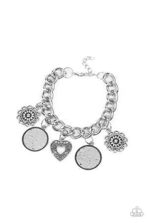collection of silver charms — including an airy heart, flowers, and textured coin-like discs — dance from a chunky silver chain around the wrist
