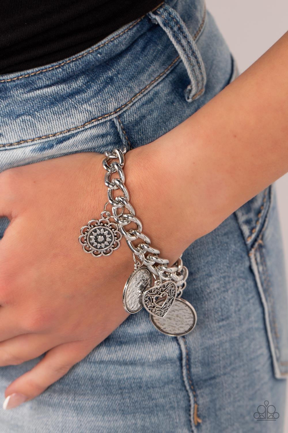 collection of silver charms — including an airy heart, flowers, and textured coin-like discs — dance from a chunky silver chain around the wrist