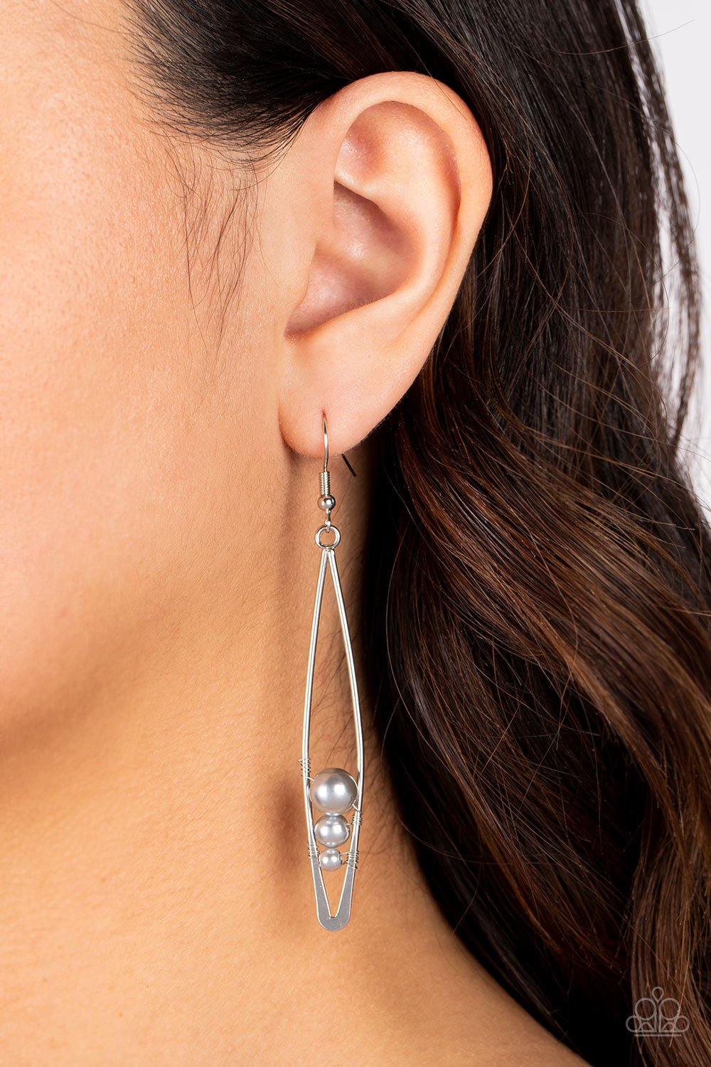 Threaded along dainty silver wires, shimmery gray pearls decrease in size as they tumble down the bottom of an elongated silver frame 